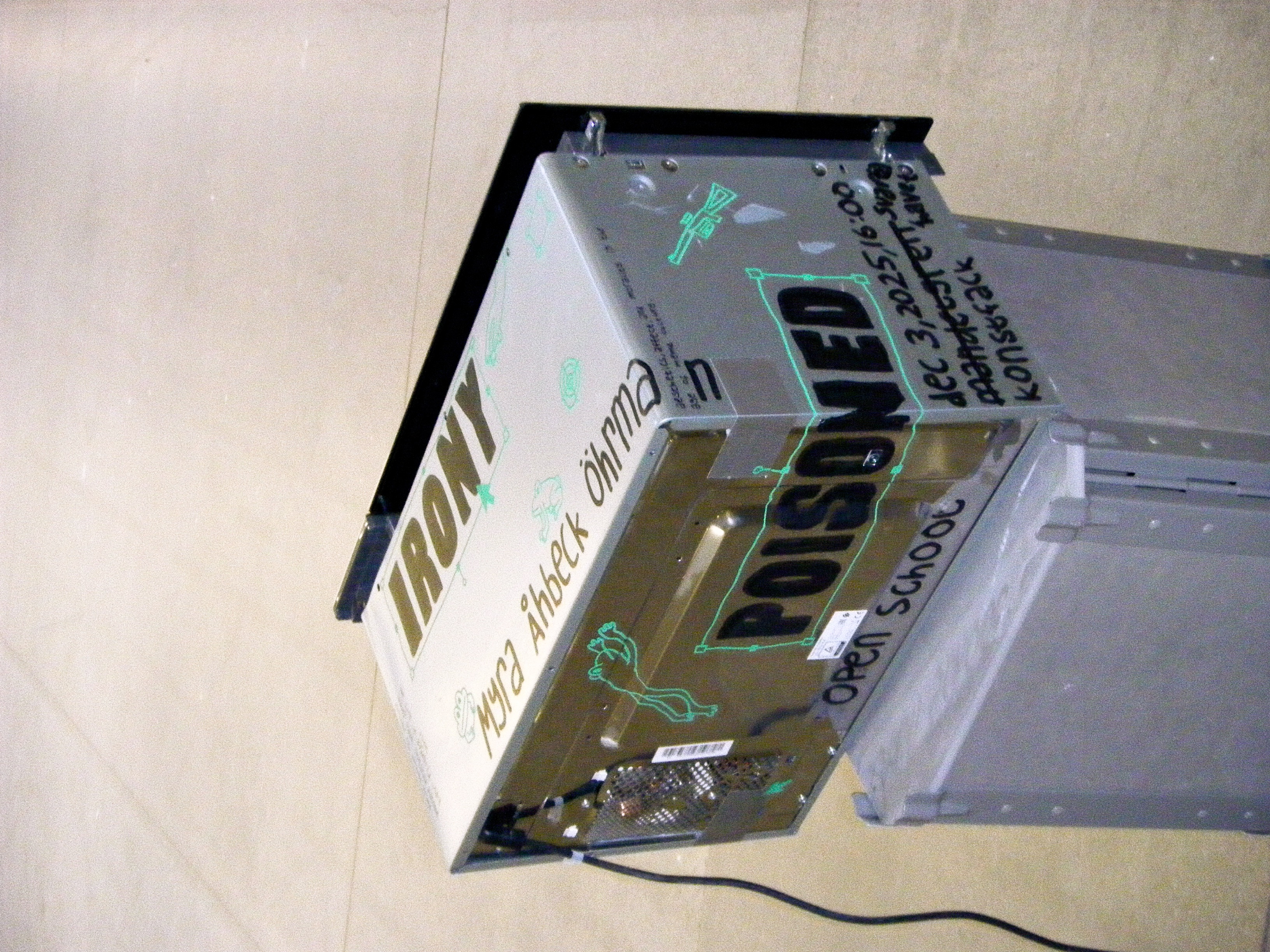 a microwave that got repurposed as a poster for myra åhbeck öhrman's lecture "irony poisoned". green frogs, graphic computer interfaces and guns are spread throughout the print.